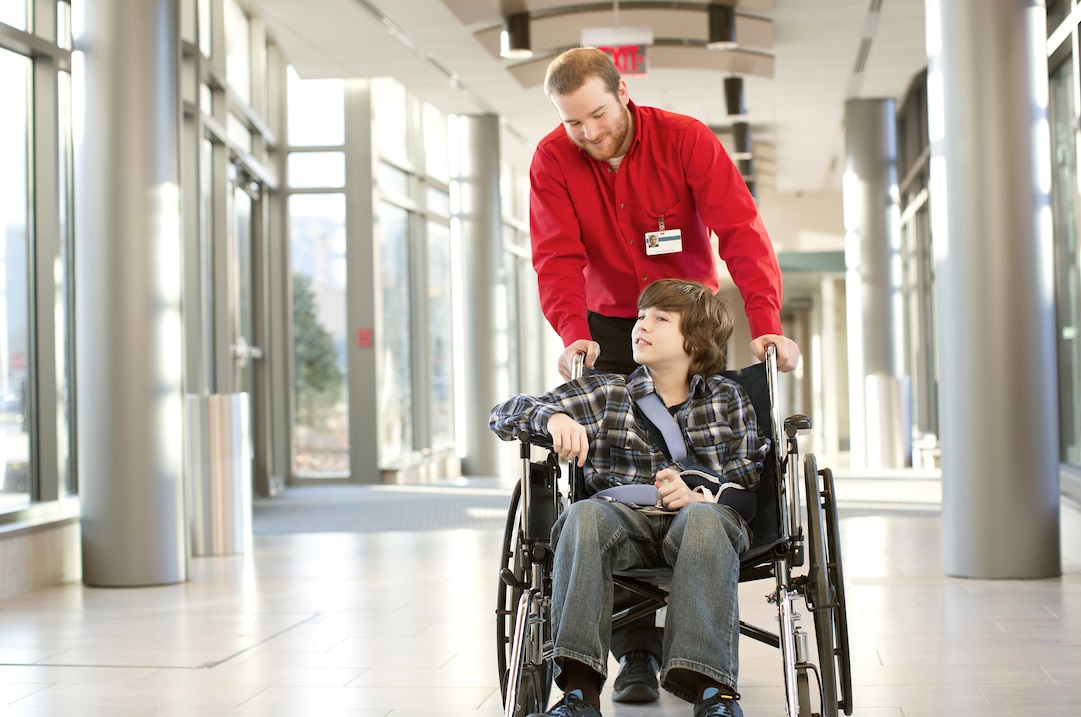 Facility worker pushing a young patient in a wheelchair.